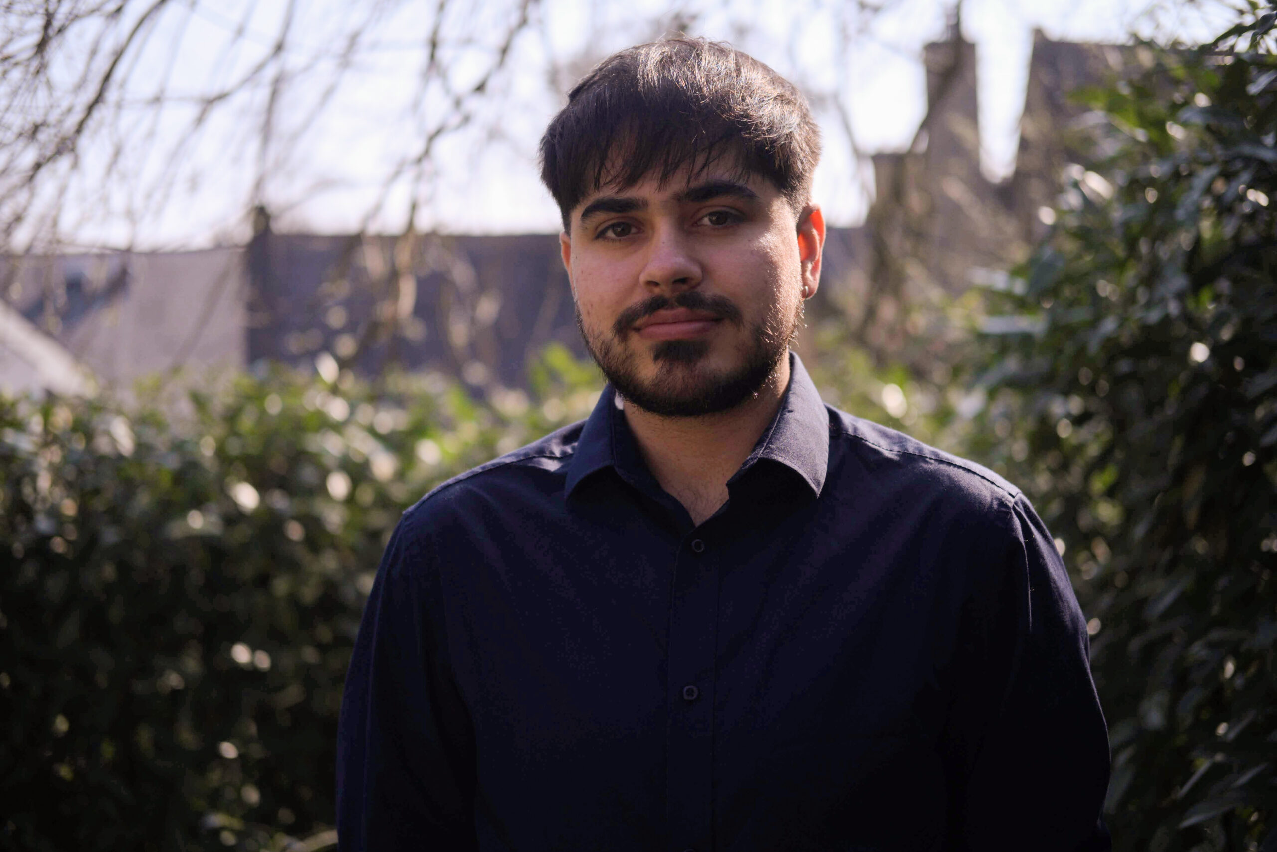 Photo of Lucas Mahal, a member of the editorial board. He is stood outside in front of a hedge and is wearing a deep purple shirt