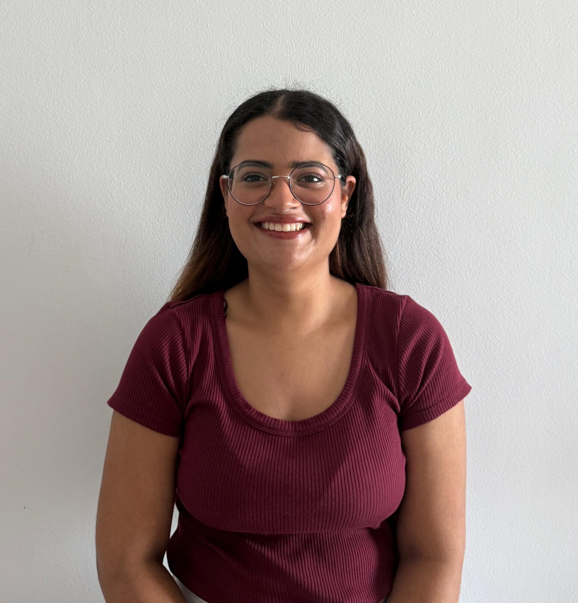 Photo of Khyati Mehta, the journal's marketing and design manager. She is smiling in front of a white wall and is wearing a maroon t-shirt.